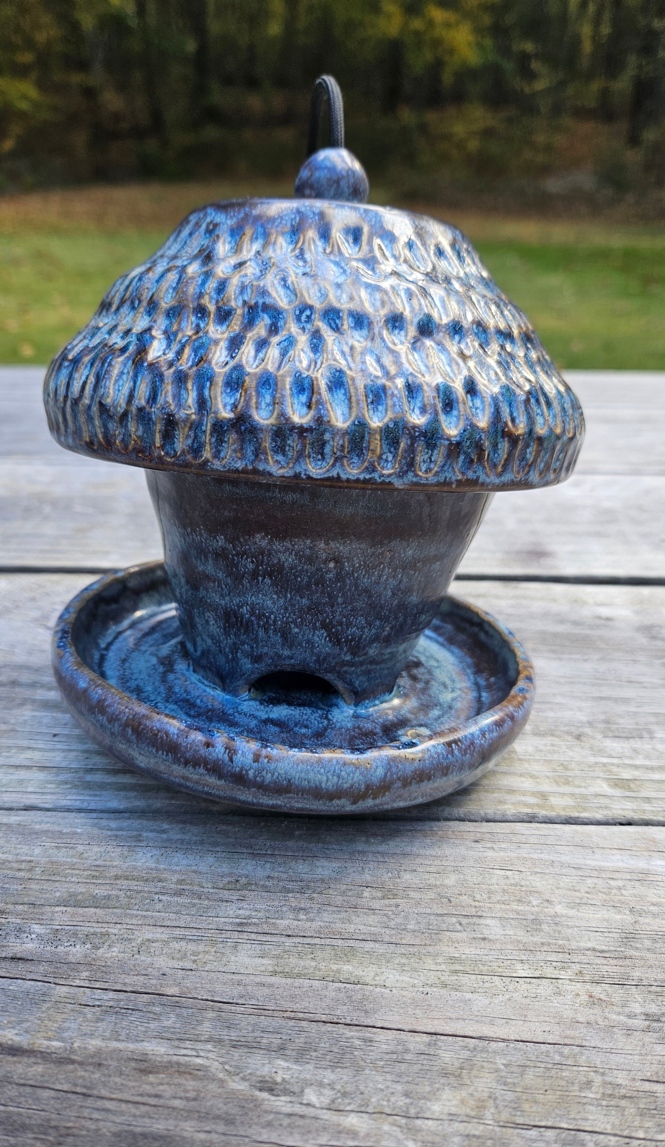 Blue ceramic bird feeder on a wooden surface with a natural background